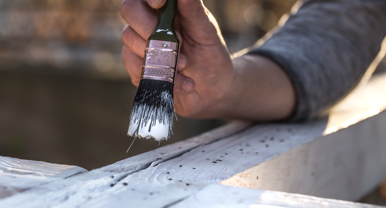 Hand applying protective sealant to a wooden surface with insect holes while pest-proofing a home